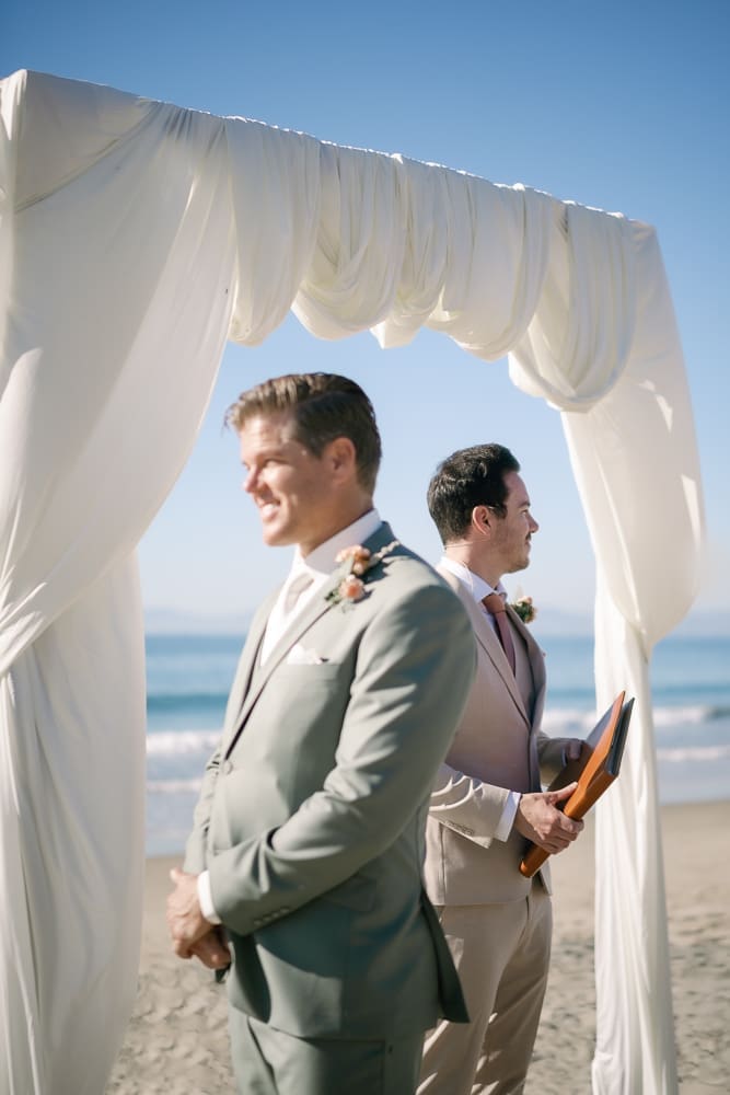 Groom waiting for bride under white drapery arch of wedding ceremony on Torrance Beach