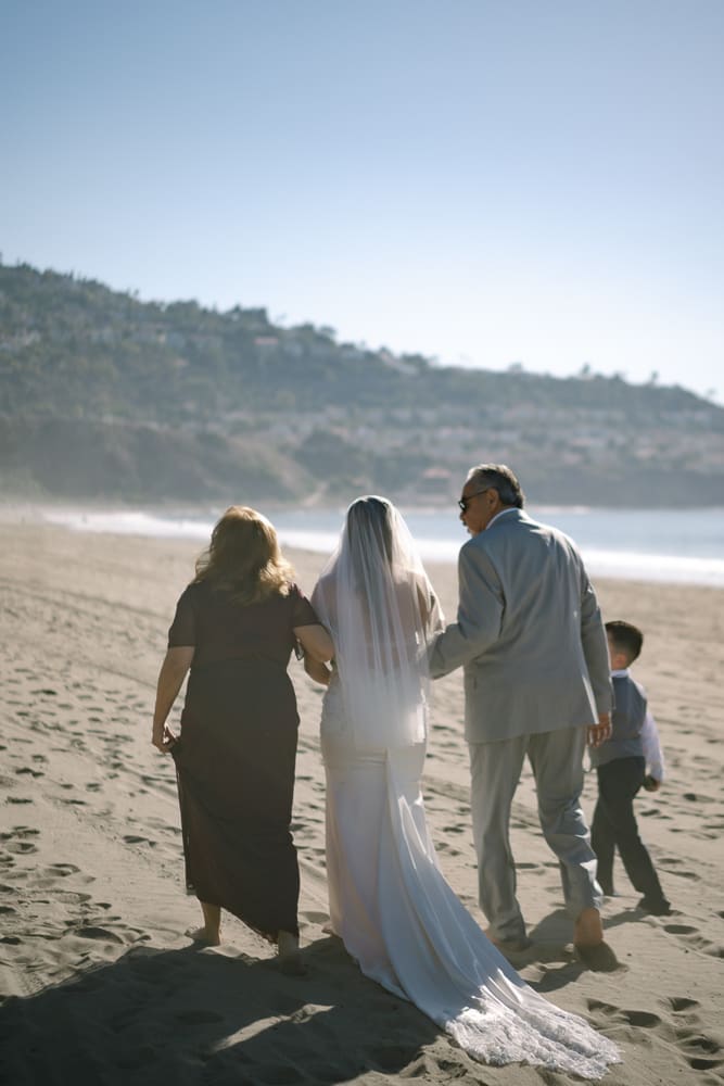 Bride walking towards wedding ceremony on Torrance Beach with parents