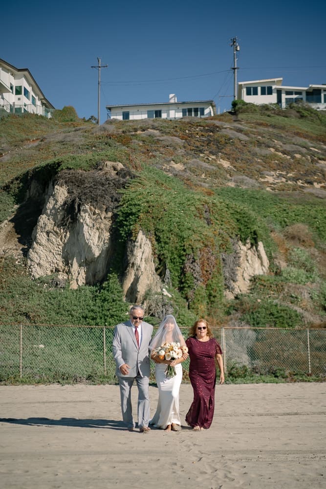 Bride walking towards wedding ceremony on Torrance Beach with parents
