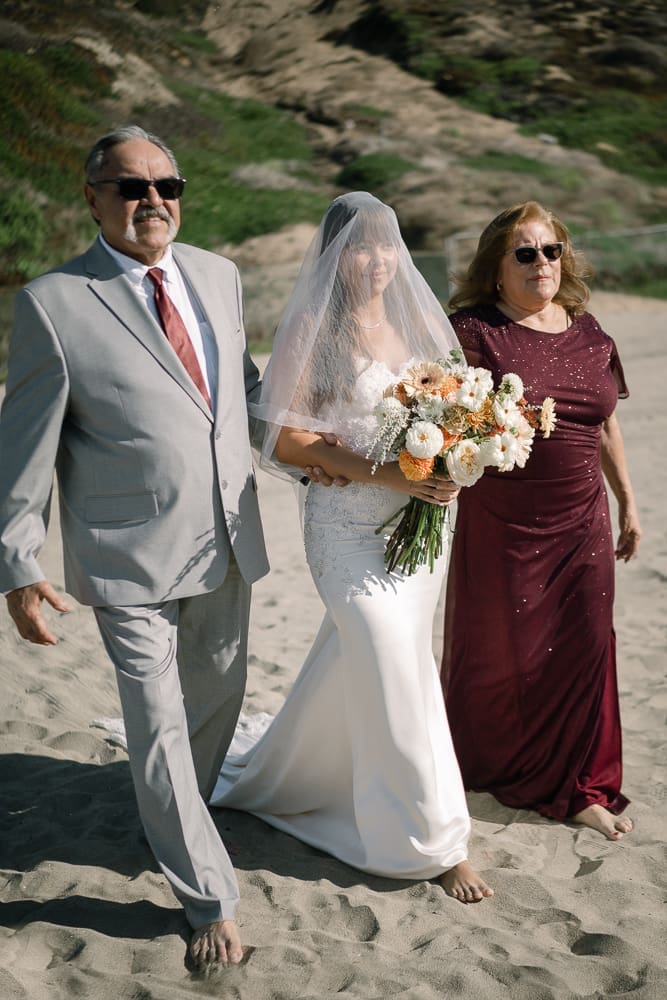 Bride walking towards wedding ceremony on Torrance Beach with parents