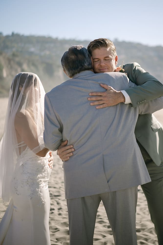 Bride watching father and groom hugging at wedding ceremony on Torrance Beach