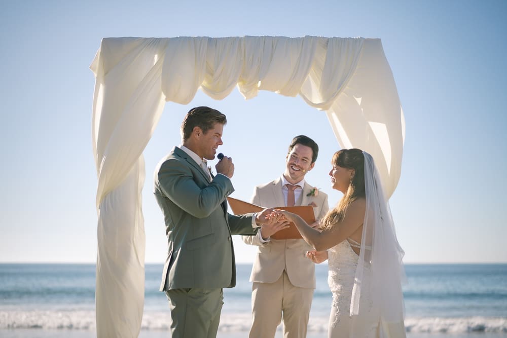 Groom saying vows holding bride's hand at wedding ceremony on Torrance Beach