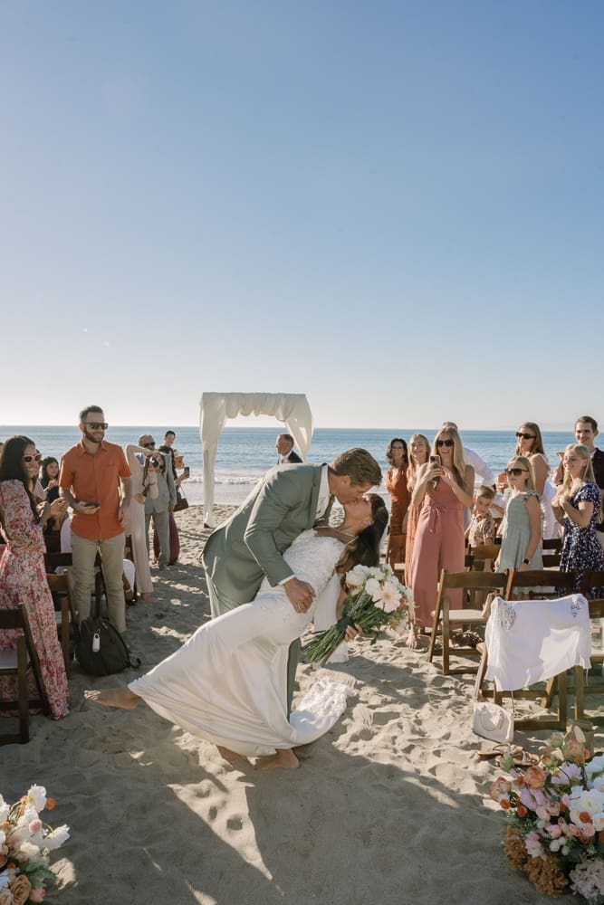 Bride and groom kissing and dipping in aisle of wedding ceremony on Torrance Beach